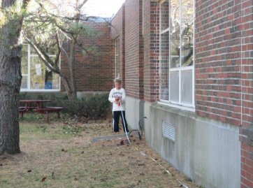 A boy with measuring tape next to brick building